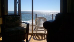 A room with a large window overlooking the ocean, featuring two chairs and a wooden deck.