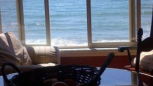 A room with a view of the ocean through large windows, a round table with a basket, and a chair.