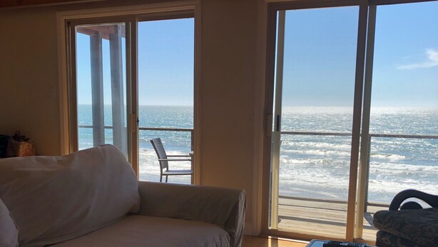 A room with a large window overlooking the sea, a sofa, and a glass coffee table.