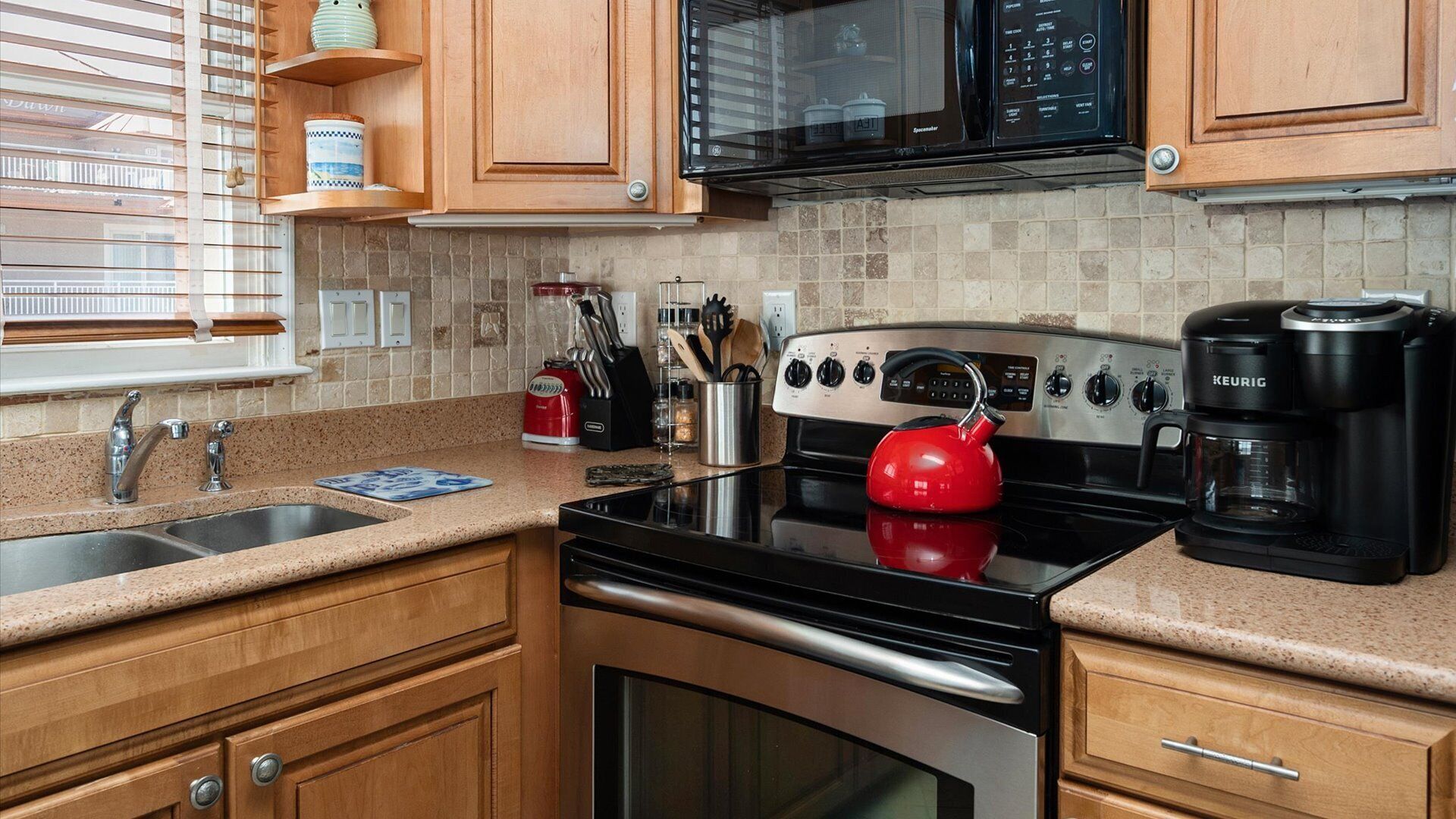 A kitchen with wooden cabinets, a stainless steel stove, a red kettle, a coffee maker, and a microwave.