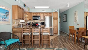 A kitchen with wooden cabinets, a central island with stools, a microwave, stove, and refrigerator.