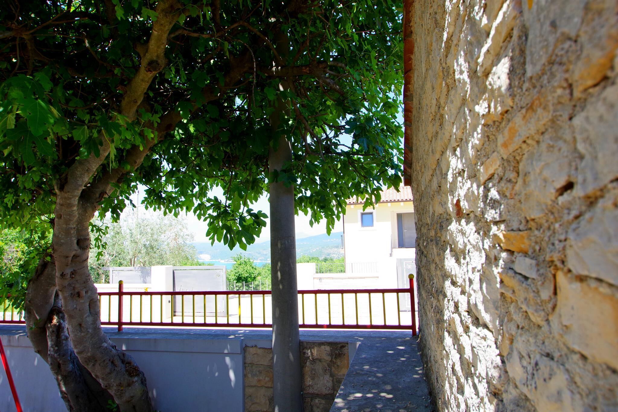 A tree-lined pathway leading to a building with a red railing and stone walls.