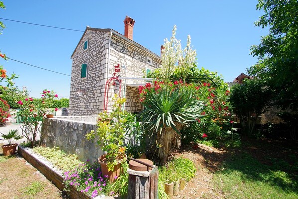 A stone building with a chimney, surrounded by a garden with various plants and flowers.