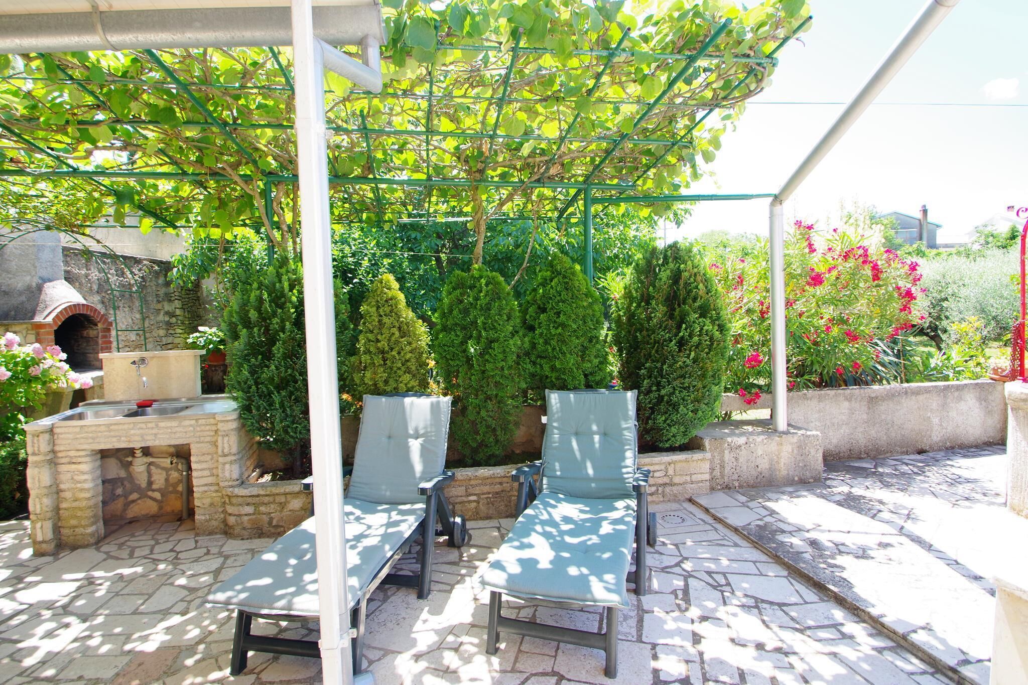 An outdoor patio with stone flooring, a brick fireplace, and two lounge chairs under a pergola.