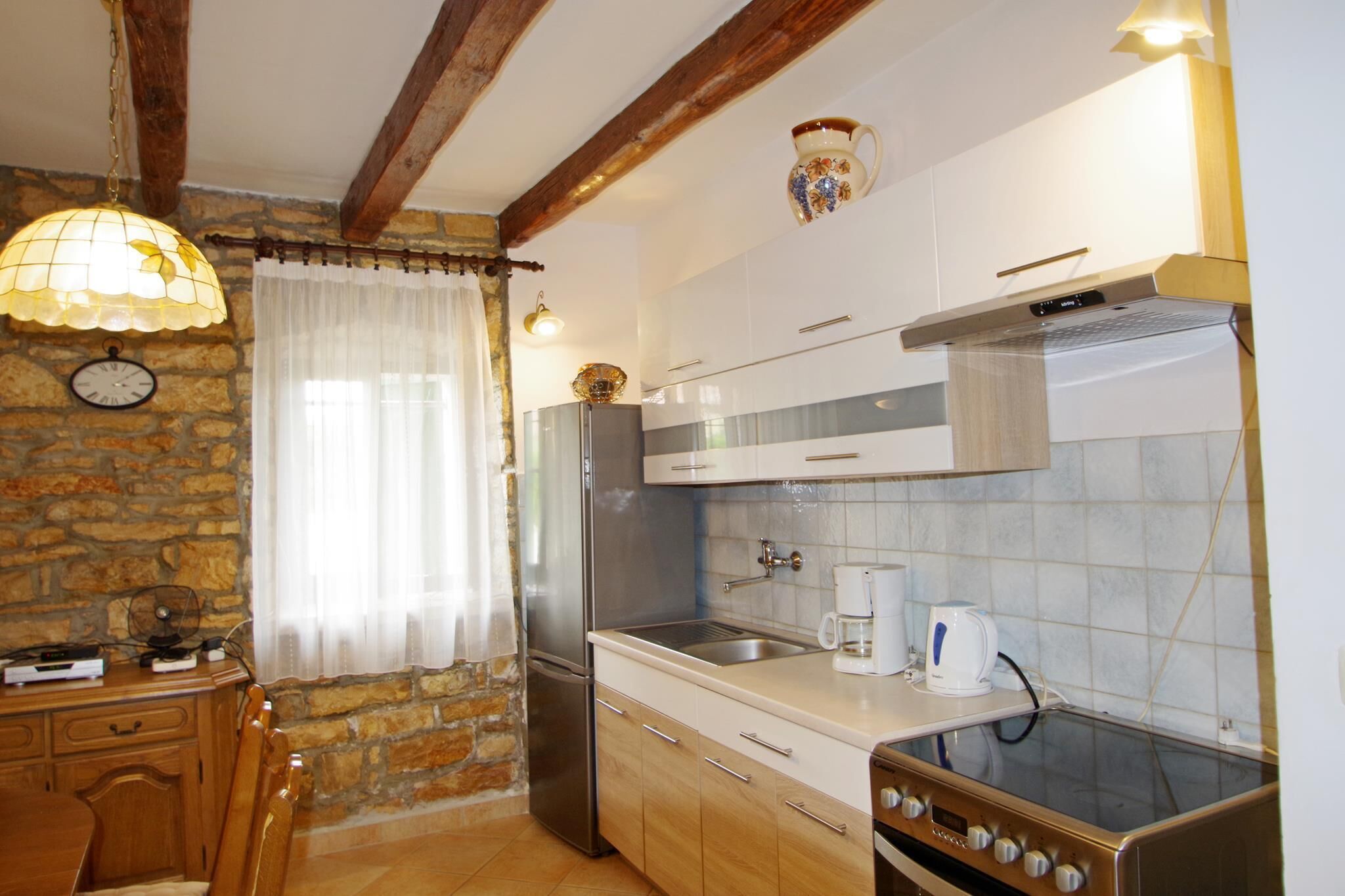 Une cuisine compacte équipée d’un réfrigérateur, d’une cuisinière et d’un évier. Il y a une horloge au mur et une fenêtre avec des rideaux.