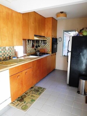 Kitchen with sink, stove, and refrigerator, featuring a window and a small rug.