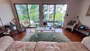 A living room with a sofa, a coffee table, a fan, and a view of a balcony with trees.