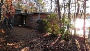 A cabin with a small porch and a covered outdoor area, surrounded by trees and a lake.