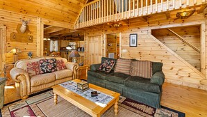 L’intérieur d’un chalet en bois, avec deux canapés, une table basse et un escalier.