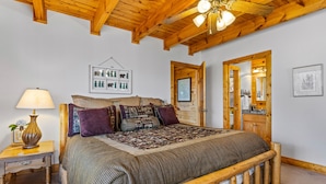 Une chambre à coucher avec un lit en bois, une table de chevet avec une lampe, un tableau encadré au mur et une porte avec un miroir.