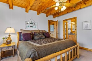 A bedroom with a wooden bed frame, a nightstand with a lamp, a framed picture on the wall, and a door with a mirror.