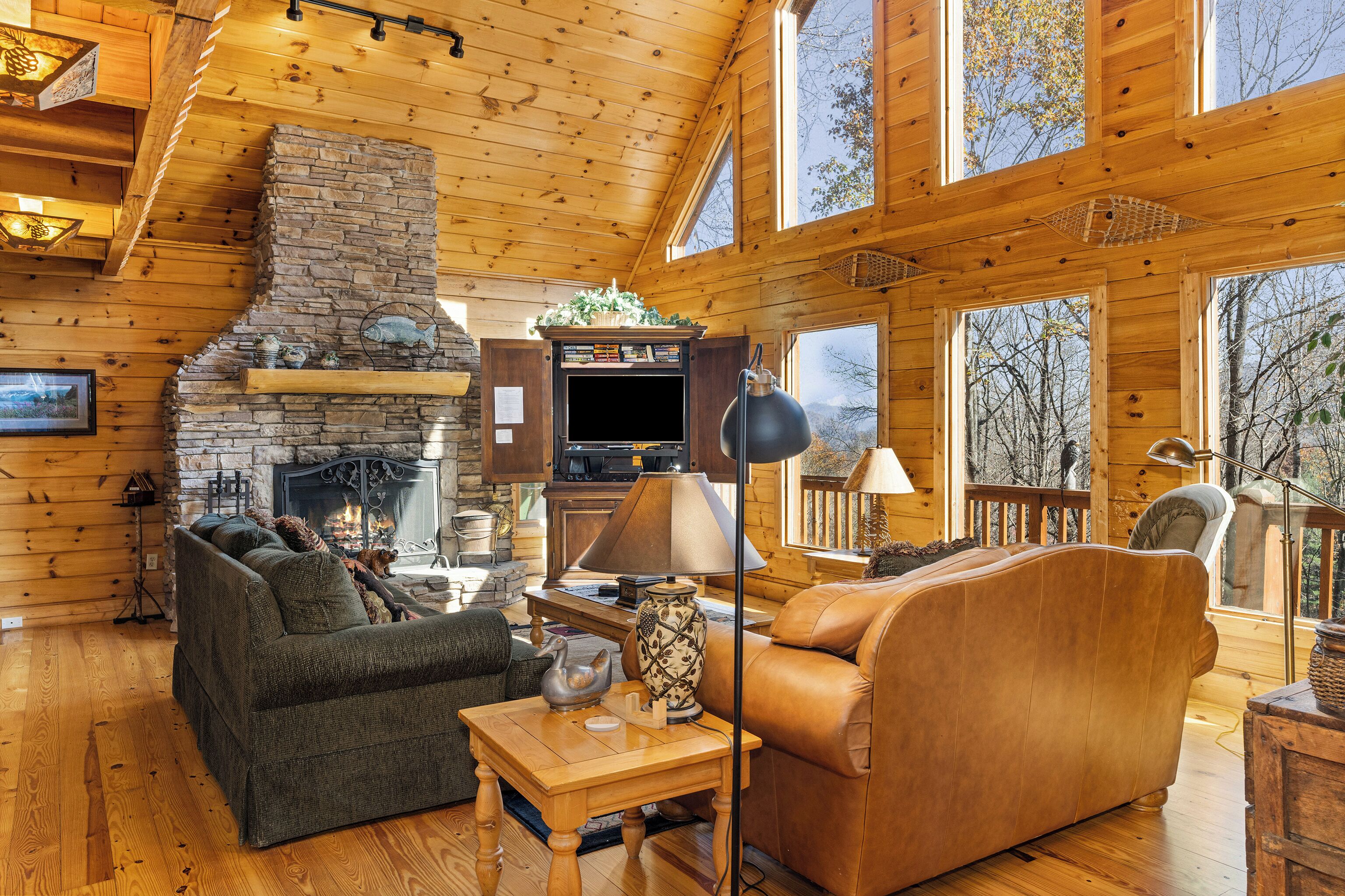 L’intérieur d’une cabane en rondins, avec une cheminée en pierre, des meubles en bois et de grandes fenêtres.