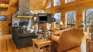 L’intérieur d’une cabane en rondins, avec une cheminée en pierre, des meubles en bois et de grandes fenêtres.