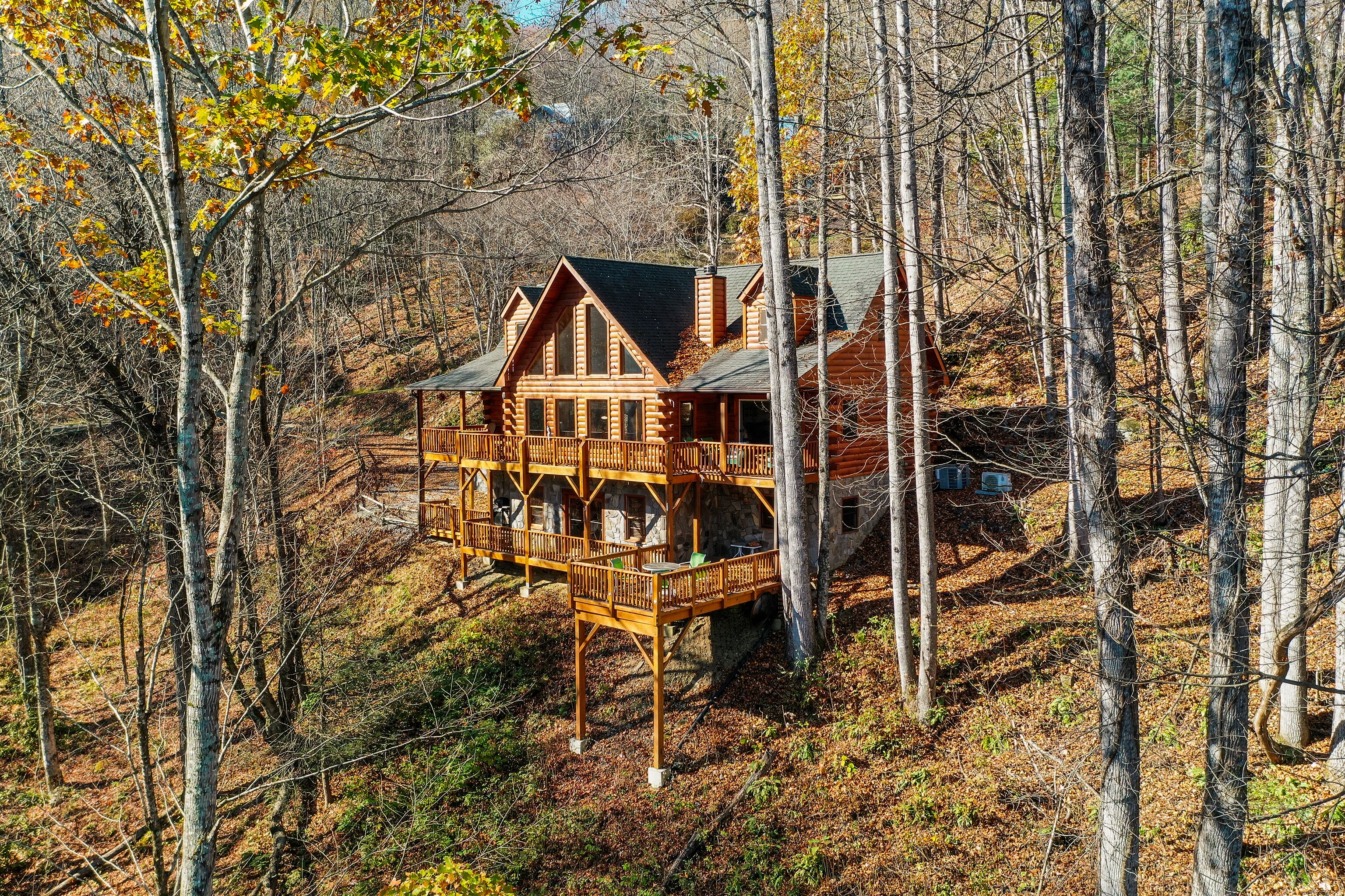 A log cabin with a multi-level deck surrounded by forest.