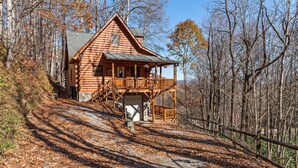 Une cabane en rondins dotée d’un porche et d’une terrasse couverte, entourée d’arbres et bordée d’un sentier de terre.
