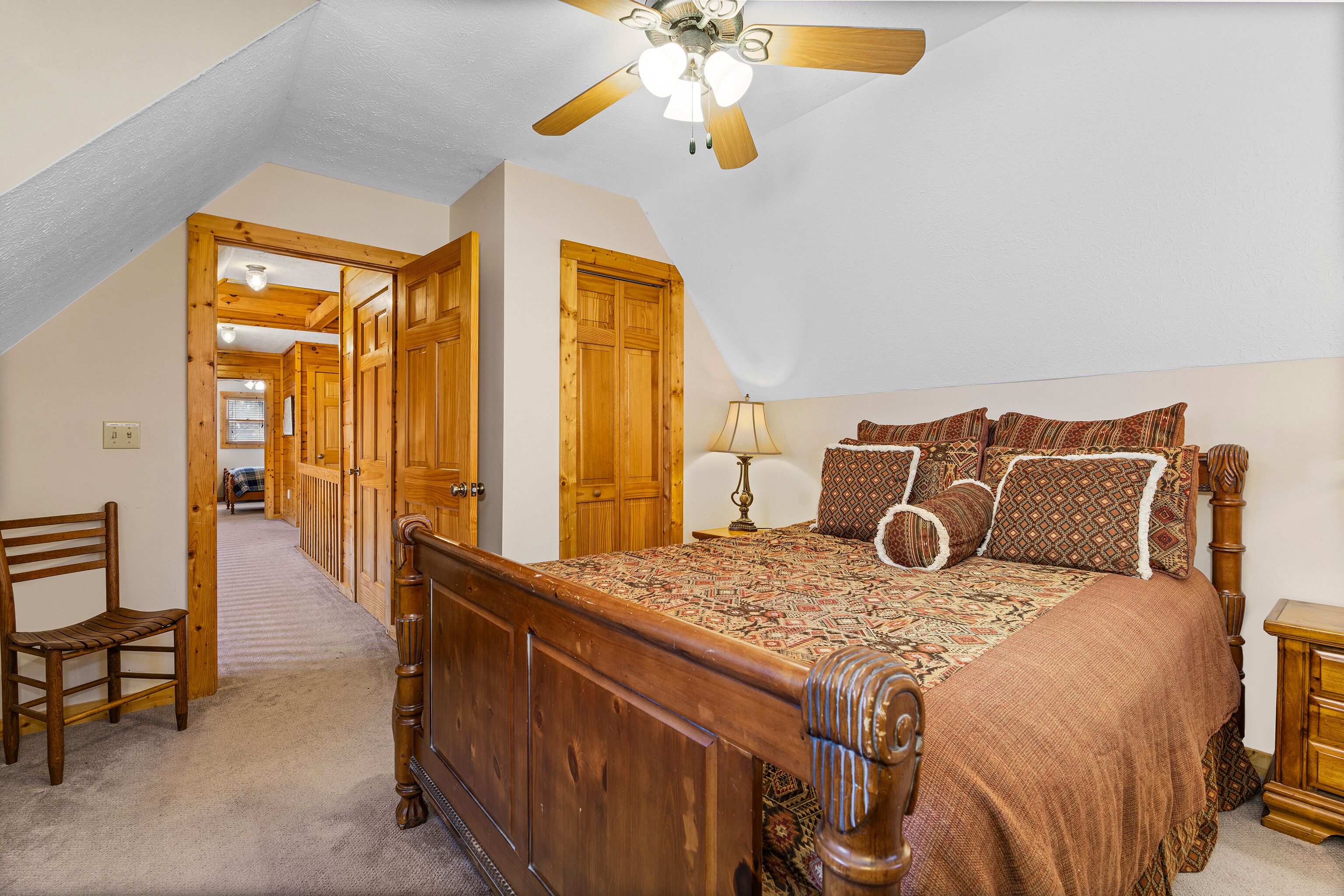 A bedroom with a wooden bed, a ceiling fan, and a carpeted floor.