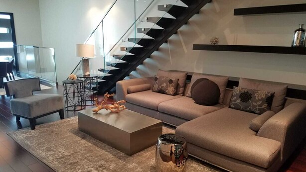Una sala de estar moderna con sofá, mesa de centro y objetos decorativos. Se ve una escalera al fondo.