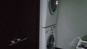 Habitación pequeña con lavadora y secadora, una mesita y una puerta.