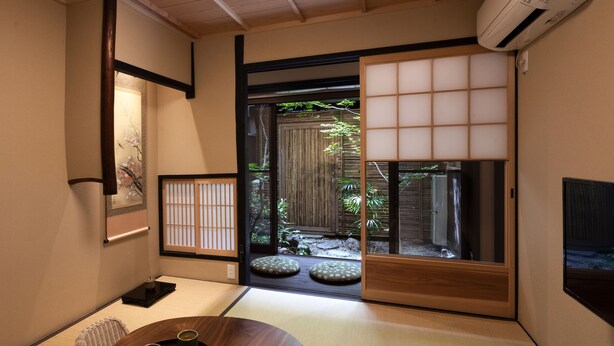 A traditional Japanese room with tatami flooring, a low table with two cups, and a sliding door leading to a garden. - Rinn Tenjincho (Kyoto)