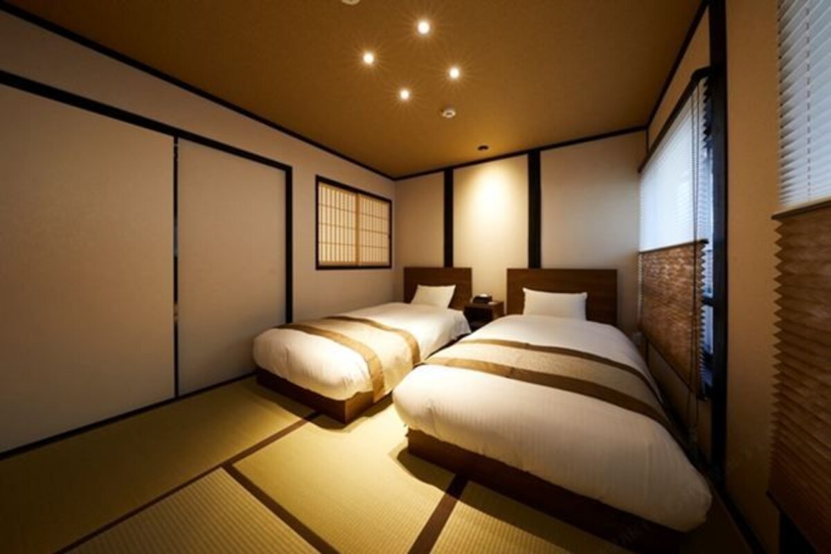 A traditional Japanese-style room with tatami flooring, two beds with wooden headboards, and a shoji screen.