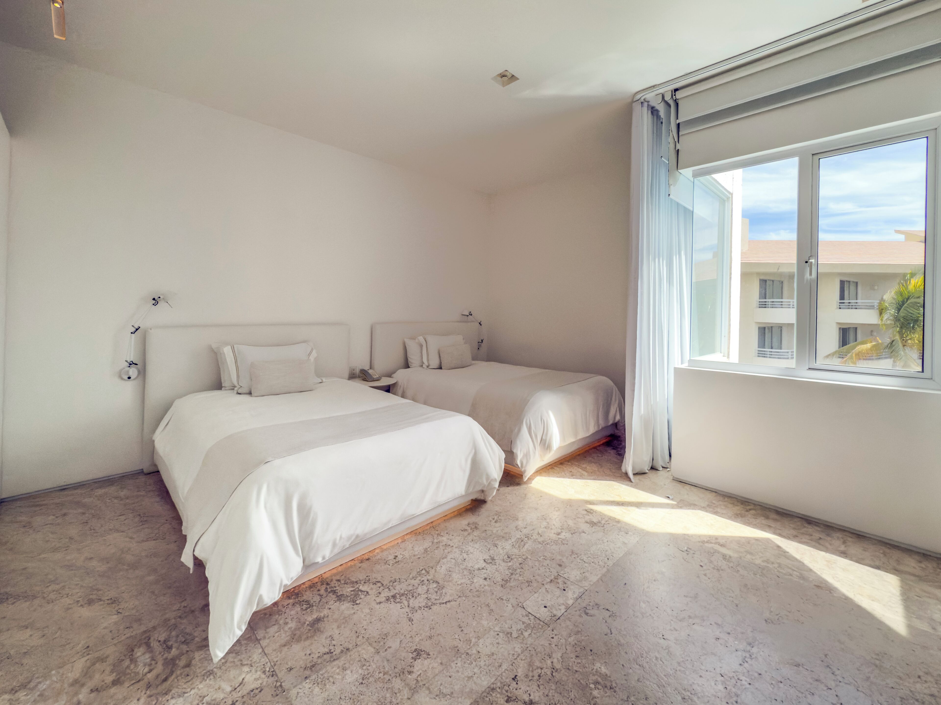 A bedroom with two beds, a large window, and a view of buildings outside.