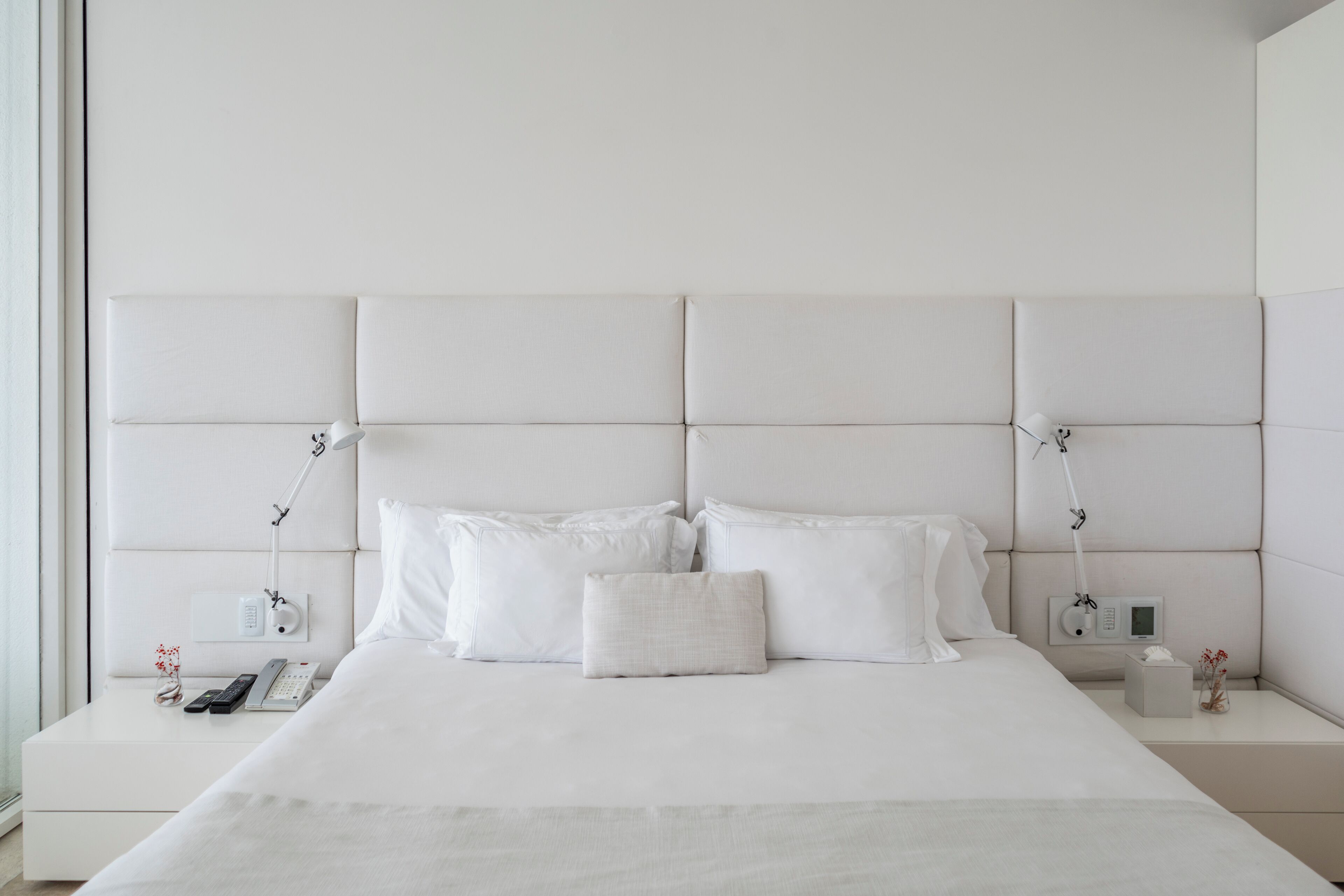 Une chambre moderne avec un grand lit, une tête de lit blanche, des tables de chevet avec des lampes et une petite table de nuit avec un téléphone et une télécommande.