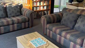 Un salon avec deux canapés à motifs, une table basse, une bibliothèque et une grande fenêtre avec des stores.