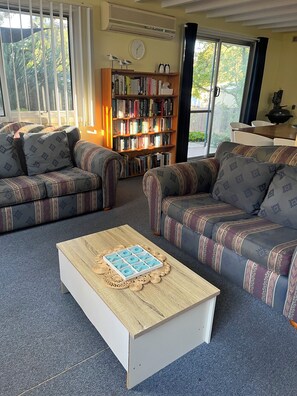 Un salon avec deux canapés à motifs, une table basse, une bibliothèque et une grande fenêtre avec des stores.