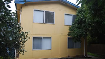 A two-story yellow building with three windows, a blue roof, and a tree in front.
