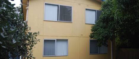 A two-story yellow building with three windows, a blue roof, and a tree in front.