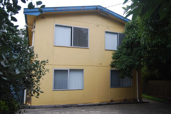 A two-story yellow building with three windows, a blue roof, and a tree in front.