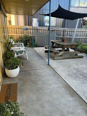 A covered patio area with a picnic table, two white chairs, and potted plants. - Ventnor Anchorage Site (Ventnor)
