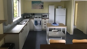 Een kleine keuken met een spoelbak, fornuis, magnetron en koelkast. Er is een raam dat natuurlijk licht biedt en een schilderij aan de muur.
