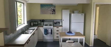 A compact kitchen with a sink, stove, microwave, and refrigerator. There's a window with a view of greenery outside.