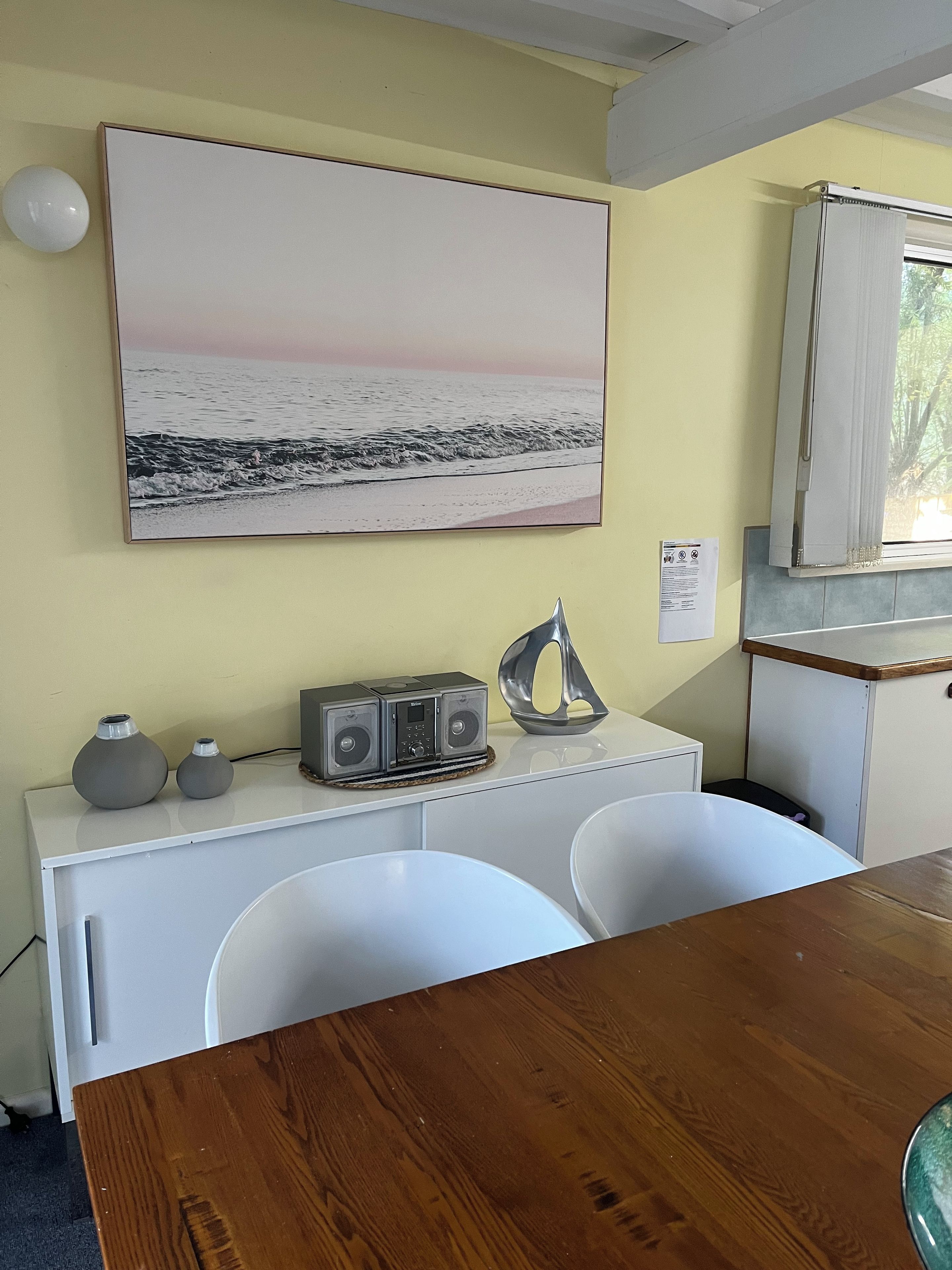A room with a white desk, a large painting of a beach, a radio, and a cabinet.