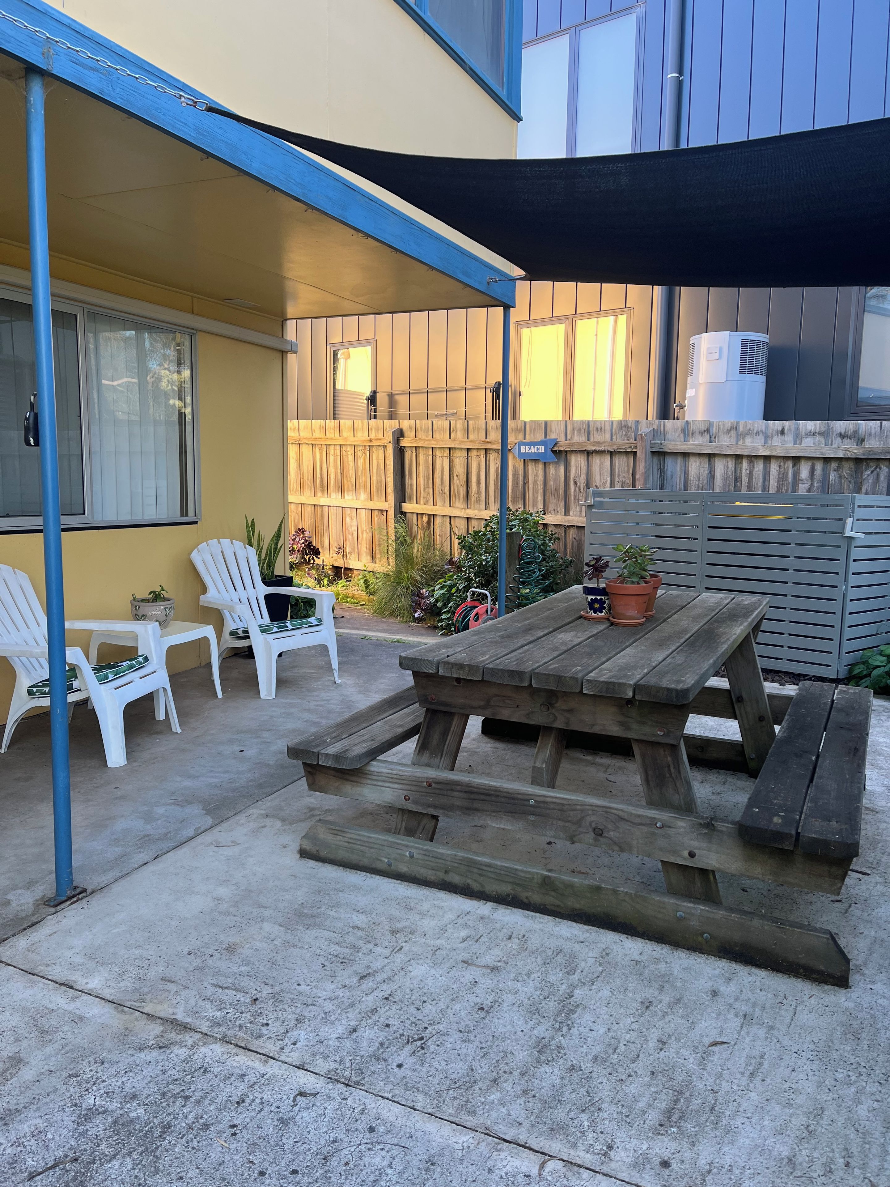 Un patio couvert avec une table et des chaises en bois, un panneau indiquant « PLAGE », et une clôture en bois.