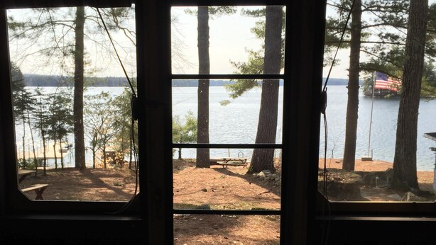 A view through a window of a cabin with a lake and trees in the background. - a rustic log cabin (Raymond)