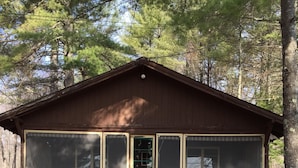 A small cabin with a wooden exterior, a front door, and two windows. - a rustic log cabin (Raymond)