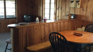 A wooden interior with a round dining table, chairs, a bench, a small bar area, and a window. - a rustic log cabin (Raymond)