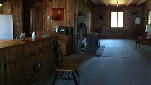 A rustic cabin interior with wooden walls, a fireplace, a bar area, and a dining table. - a rustic log cabin (Raymond)