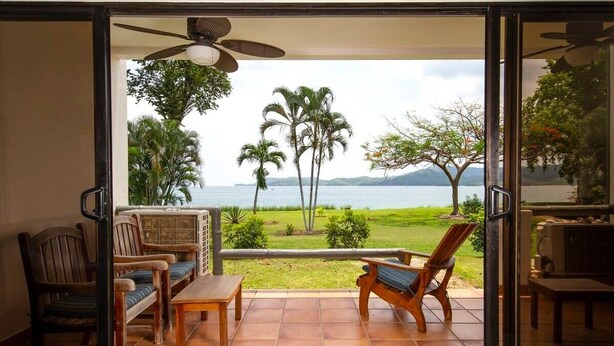 A balcony with a view of the sea, featuring wooden furniture and a ceiling fan. - Newly Remodeled Beachfront Condo, Ground-Floor Terrace & Direct Access to Playa Flamingo (Santa Cruz, Guanacaste, Playa Flamingo)
