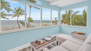 Une pièce avec vue sur la plage, une table basse en bois avec des livres et un canapé blanc.
