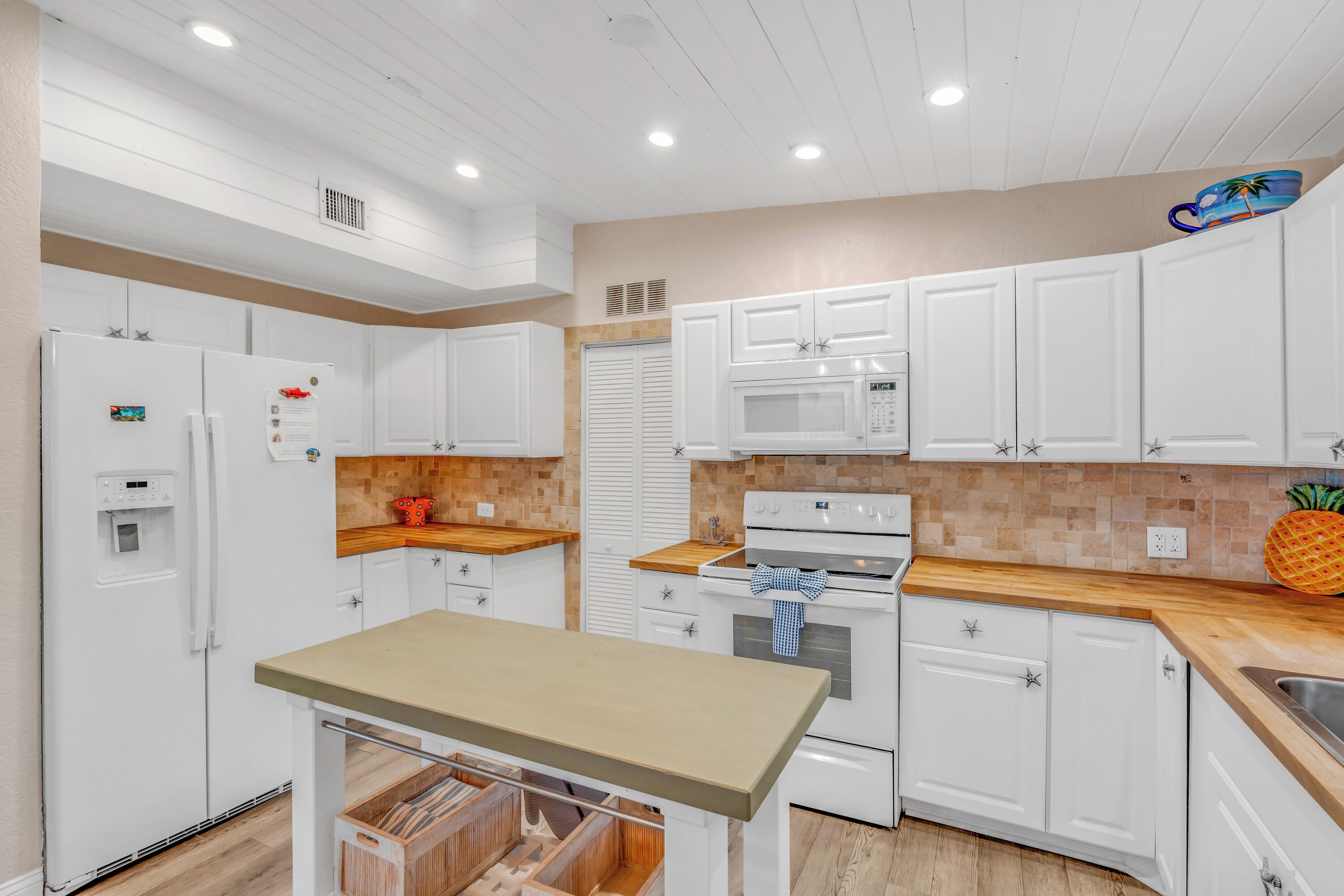 A modern kitchen with white cabinets, a wooden countertop, a built-in oven, and a microwave.