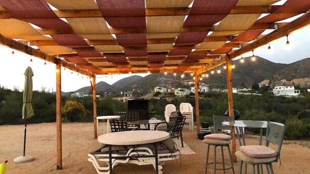 An outdoor patio with a wooden pergola, string lights, and a view of the surrounding landscape. - Labios Tintos Bungalow, Valle de Guadalupe, BC, México (Las Lomas)
