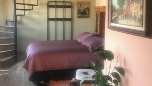A bedroom with a bed, a wooden staircase, a ceiling fan, a framed painting, and a small table with a plant. - Labios Tintos Bungalow, Valle de Guadalupe, BC, México (Las Lomas)
