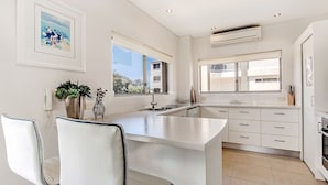 A modern kitchen with a central island, white cabinetry, and a large window providing natural light. - Aarons Villa - Waterfront Perfectly located on Gympie Terrace (NOOSAVILLE)
