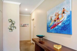 Un pasillo con un cuadro de surfistas, un adorno en la pared y un banco con un cuenco.