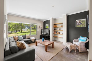 Un salon moderne avec un canapé, une table basse, un téléviseur et un fauteuil en osier.