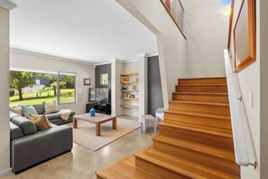 A modern living room with a sofa, coffee table, and TV, a staircase, and a view of a garden.