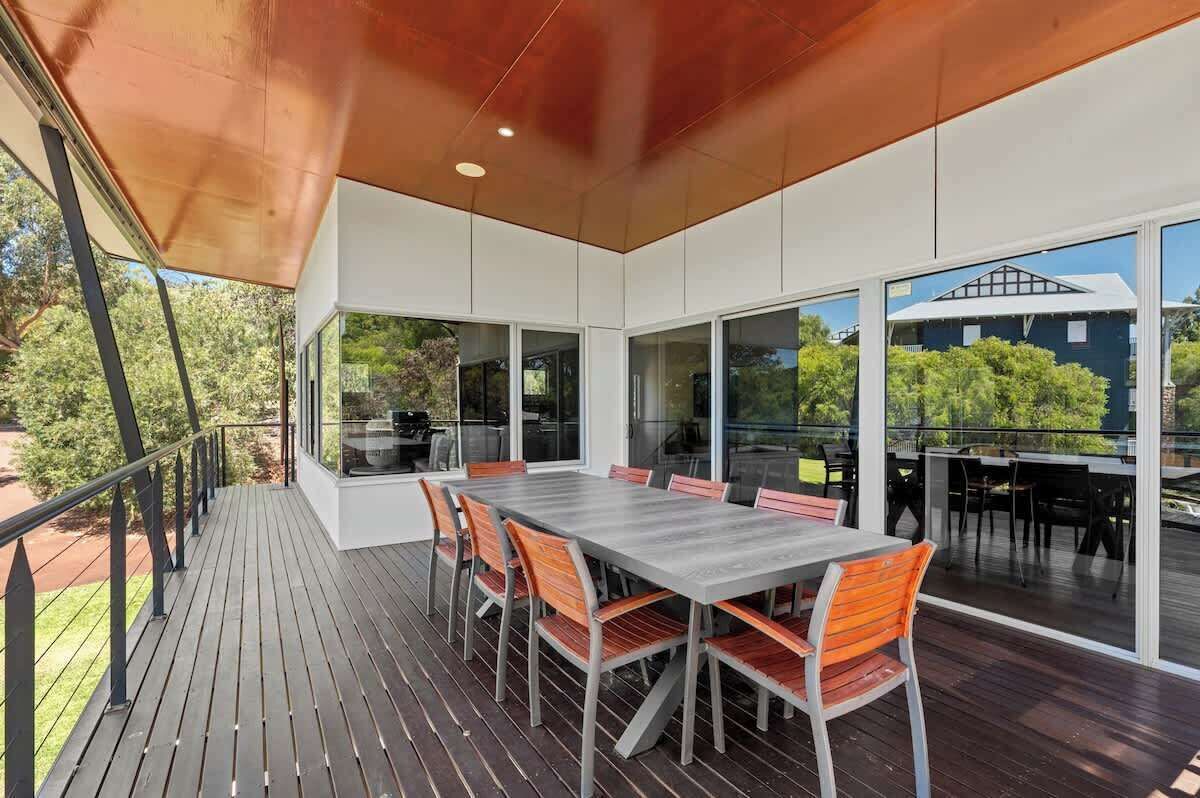 A covered outdoor dining area with a table and chairs, large windows, and a view of the surrounding greenery.